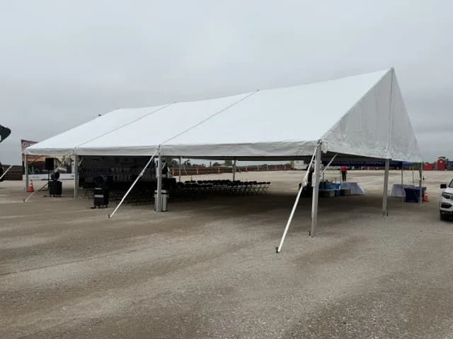 Rows of black folding chairs set up under a 40x60 frame tent for a groundbreaking ceremony