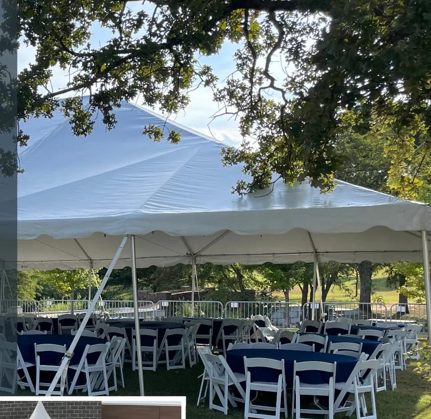 Frame tent with round tables, navy linens and white folding chairs on a lawn