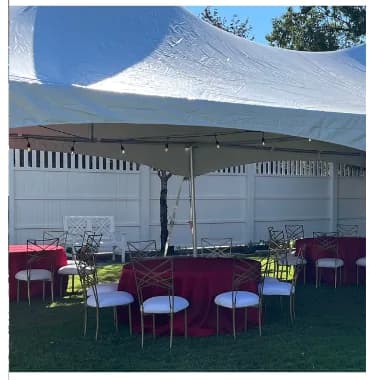 Round tables with red linens and gold chairs under a high peak tent