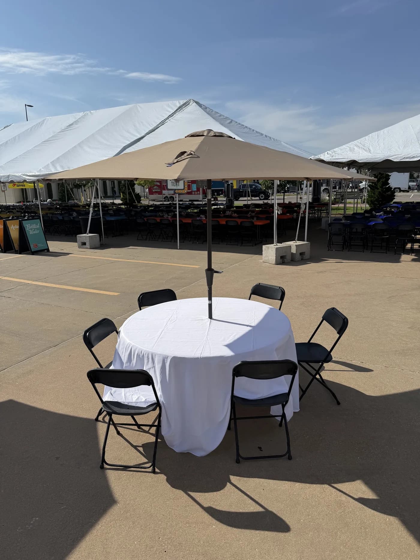 Round table rental with white linen, umbrella and black folding chairs at an outdoor event